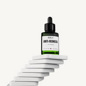 REBELX Anti-Redness Phyto Serum in green glass dropper bottle displayed on white geometric platforms, 1 fl oz size